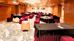 A well-lit conference room at Pride Plaza Ahmedabad, featuring a U-shaped arrangement of tables with red tablecloths, suitable for meetings and presentations.
